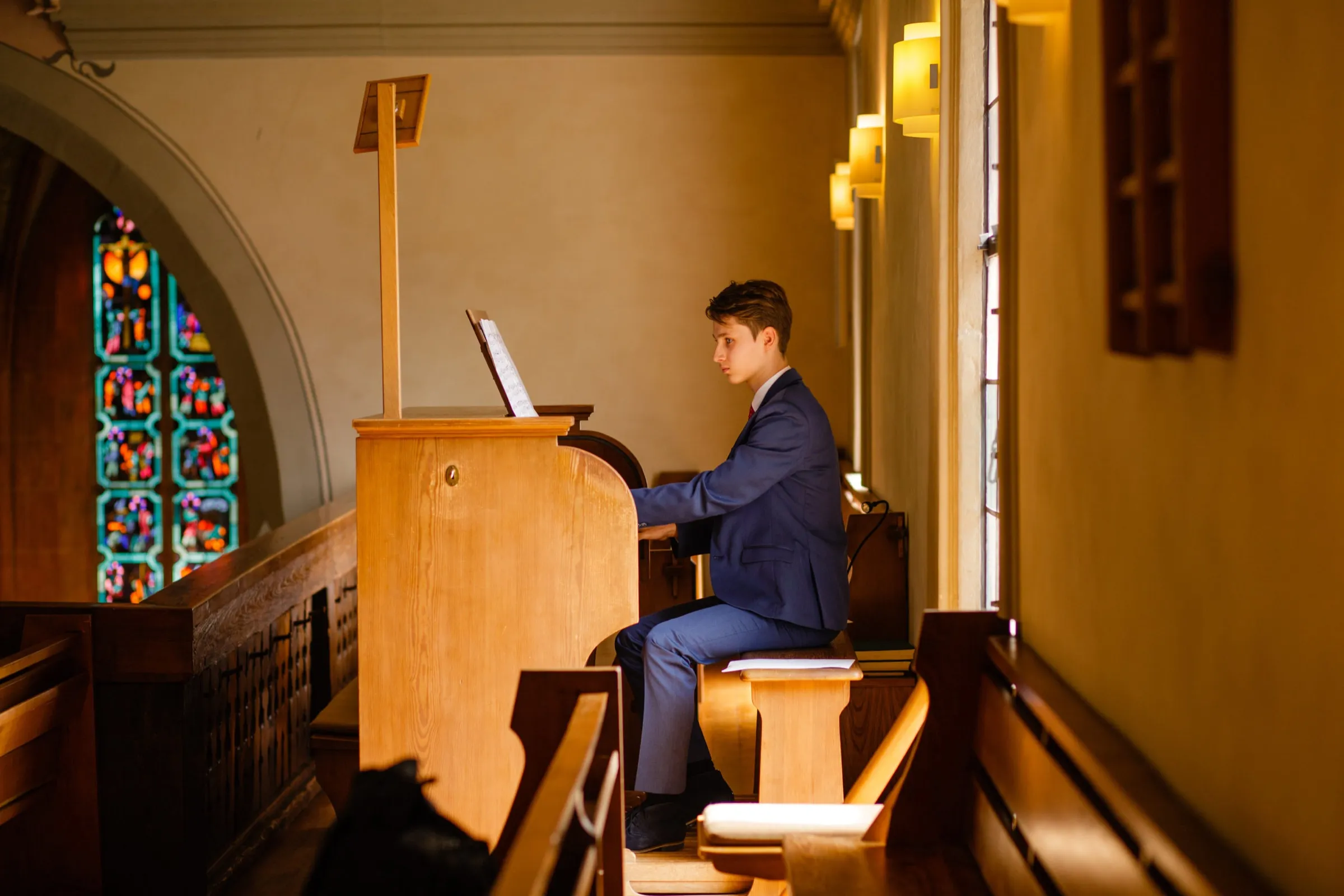Lukas Höver am Spieltisch einer Orgel auf der Empore, daneben ein Buntglasfenster