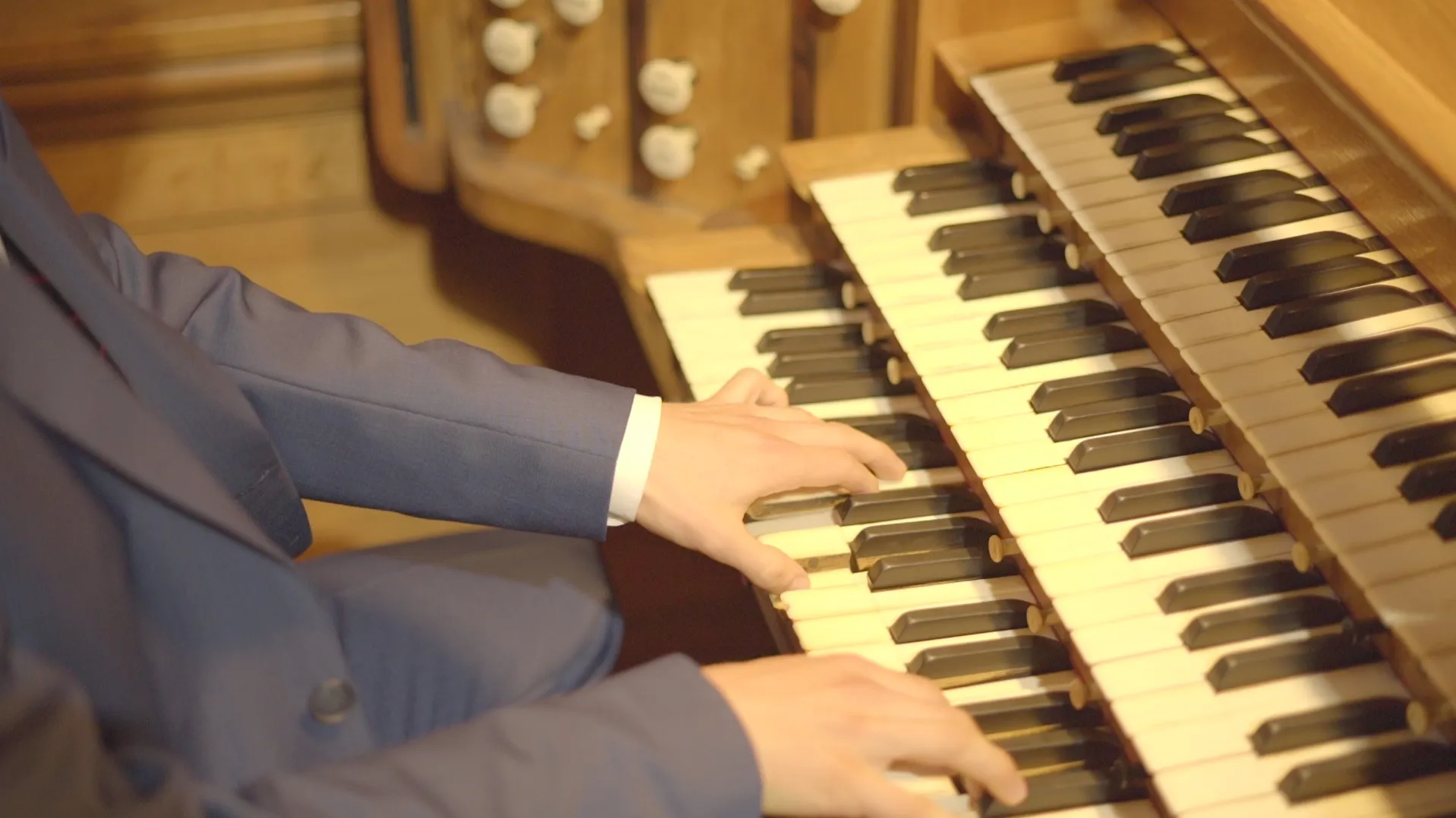 Hands on the manuals of an organ, the stop knobs visible behind them